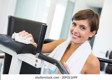 Fit Brunette Wiping Down Bench Smiling At Camera At The Gym