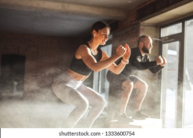 Fit caucasian couple doing squats on boxes in a crossfit style gym, well lit by bright sunlight. - Powered by Shutterstock