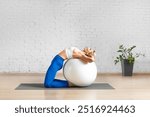 Fit Caucasian woman stretches her back while kneeling on a fitness ball in loft studio indoor. Training, pilates, props, balance, workout, gymnastics, sport concept.