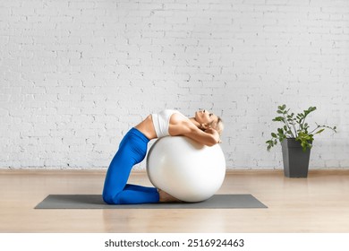 Fit Caucasian woman stretches her back while kneeling on a fitness ball in loft studio indoor. Training, pilates, props, balance, workout, gymnastics, sport concept. - Powered by Shutterstock