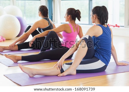 Fit class doing the half spinal twist pose on mats at yoga class in fitness studio