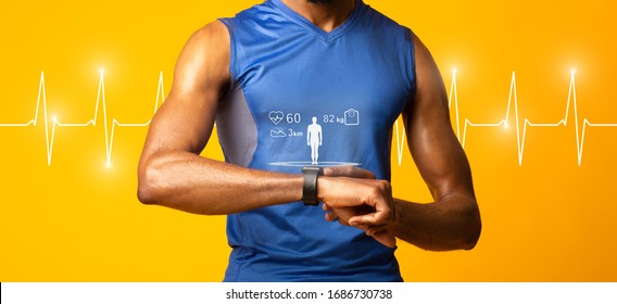 Fit Concept. Black muscular man checking fitness tracker, yellow studio wall, panorama, heart beat line in the background - Powered by Shutterstock