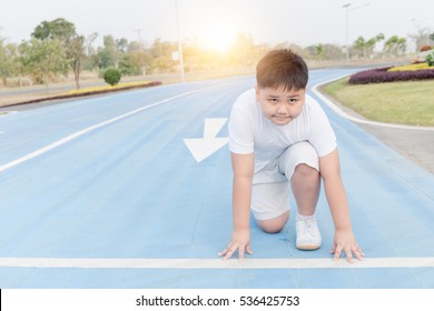 Fit And Confident Fat Boy In Starting Position Ready For Running. Kid Athlete About To Start A Sprint Looking At Camera With Bright Sunlight.