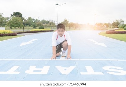 Fit And Confident Fat Boy In Starting Position Ready For Running. Kid Athlete About To Start A Sprint Looking At Camera With Bright Sunlight.