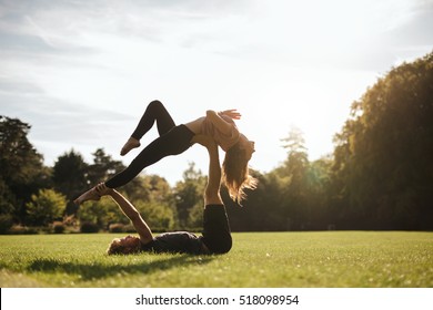 Fit Couple Doing Acrobatic Yoga Exercise In Park. Man Lying On Grass And Balancing Woman.