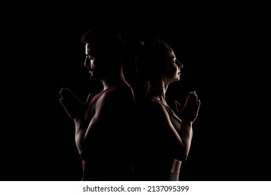 Fit Couple Posing Together. Boy And Girl Praying Back To Back Side Lit Silhouettes On Black Background.