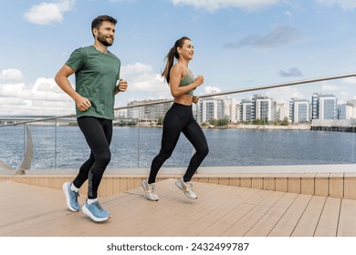 Fit couple running together on a wooden boardwalk by the river with urban skyline. - Powered by Shutterstock