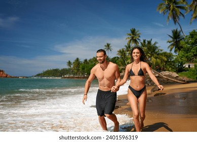 Fit couple runs joyfully on tropical beach, man, woman exercise in swimwear. Attractive duo enjoys beachfront jog, showcasing fitness, holiday travel. Morning workout beside sea, healthy lifestyle. - Powered by Shutterstock