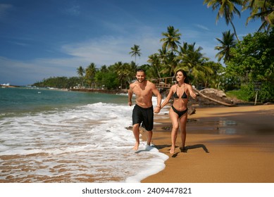 Fit couple runs on sandy beach by the sea, surrounded by palm trees. Muscular man and slender woman enjoy oceanfront run. Active lifestyle, couple's workout, beach jogging in tropical paradise. - Powered by Shutterstock