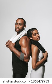 Fit Couple Standing With Back Against Each Other. Fit Man And Woman Relaxing After Workout Listening To Music Holding Towel.