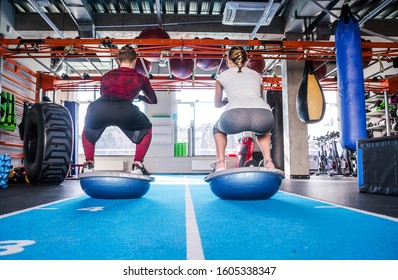 Fit Couple Working On Bosu Ball In Fitness Studio. Doing A Squat Exercise