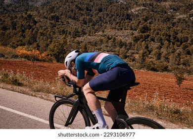Fit cyclist riding on  time trial bicycle. Side photo of man wearing cycling kit and white helmet.Sport goal achieving. Extremely strong motivated person preparing for a triathlon competition.Spain
