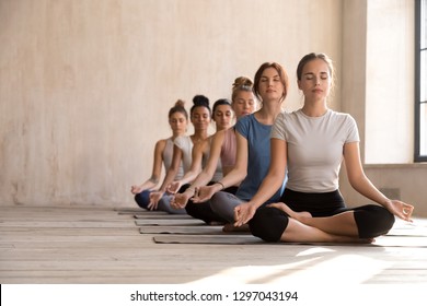 Fit diverse calm yogi sit in row meditating in lotus position in bright fitness studio, toned multiracial women practice yoga with eyes closed on rubber mats, keep mudra hands. Healthy life concept - Powered by Shutterstock