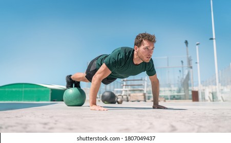 Fit exercises man strength training core doing balance push-ups workout at outdoor gym balancing on stability medicine ball with legs. Bodyweight pushups exercises. Push-up variation.