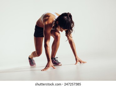 Fit Female Athlete Ready To Run Over Grey Background. Female Fitness Model Preparing For A Sprint.