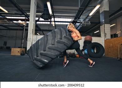 Fit female athlete working out with a huge tire, turning and flipping in the gym. Crossfit woman exercising with big tire.