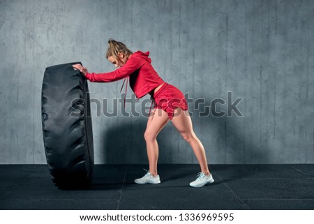 Fit female athlete working out with a huge tire. Side view. Sportswoman doing an strength exercise training.