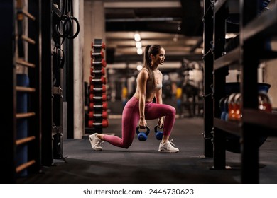 A fit female bodybuilder is doing lunges with kettlebells in a gym. - Powered by Shutterstock