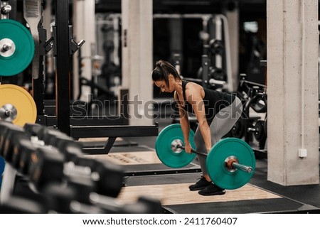 A fit female bodybuilder is exercising with barbell in a gym.