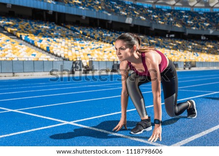 fit female runner in start position on running track at sports stadium