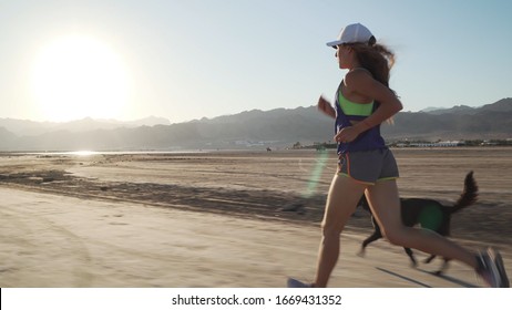 Fit Female Runs With Her Funny Dog In Dry Desert At Sunrise Rapid Slow Motion.