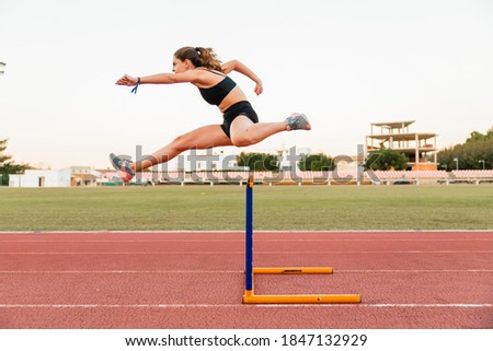 Fit female teenager athlete hurdler running jumping over hurdles