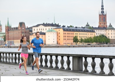 Fit Fitness Exercise People, Healthy Runners Running In Stockholm City Cityscape Skyline. Riddarholmskyrkan Church In The Background, Sweden, Europe. Healthy Multiracial Young Adults.