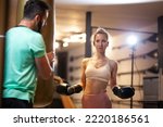 Fit girl with boxing gloves. Male fitness instructor with a female client practicing kickbox with puncing bag in a fitness studio.