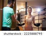 Fit girl with boxing gloves smiling. Male fitness instructor with a female client practicing kickbox with puncing bag in a fitness studio.