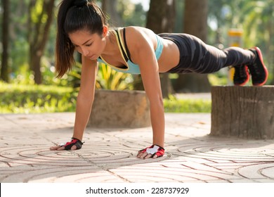 Fit girl doing straight arm plank exercise, her legs on stump