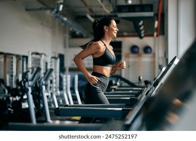 A fit girl dressed in a black sports outfit, running on a treadmill, at the gym.