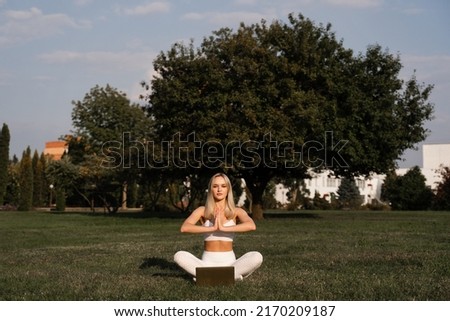 Fit girl is sitting in lotus position and meditating online with laptop. Meditation and relaxation outdoors