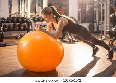 Fit girl workout with fitness ball in plank position in gym.