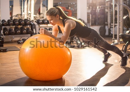 Fit girl workout with fitness ball in plank position in gym.