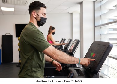 Fit Guy Wearing Face Mask Adjusting Settings On Gym Treadmill During Pandemic