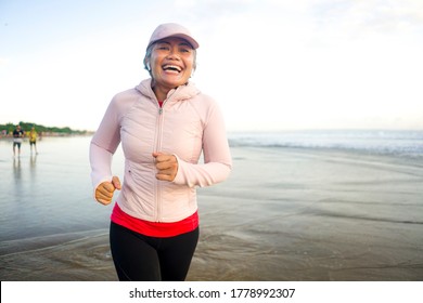 Fit And Happy Middle Aged Woman Running On The Beach - 40s Or 50s Attractive Mature Lady With Grey Hair Doing Jogging Workout Enjoying Fitness And Healthy Lifestyle At Beautiful Sea Landscape