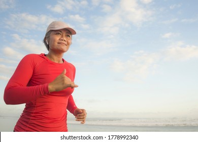 Fit And Happy Middle Aged Woman Running On The Beach - 40s Or 50s Attractive Mature Lady With Grey Hair Doing Jogging Workout Enjoying Fitness And Healthy Lifestyle At Beautiful Sea Landscape