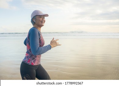 fit and happy middle aged woman running on the beach - 40s or 50s attractive mature lady with grey hair doing jogging workout enjoying fitness and healthy lifestyle at beautiful sea landscape