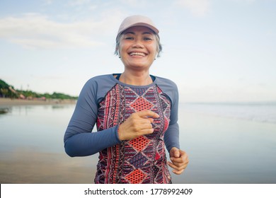 Fit And Happy Middle Aged Woman Running On The Beach - 40s Or 50s Attractive Mature Lady With Grey Hair Doing Jogging Workout Enjoying Fitness And Healthy Lifestyle At Beautiful Sea Landscape