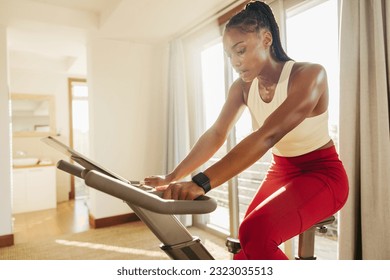 Fit and healthy African woman maintains her active lifestyle by incorporating a stationary bike into her regular exercise routine, striving to stay healthy and strong.