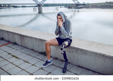 Fit healthy caucasian handicapped sportsman with artificial leg and hoodie on head sitting on quay and resting. - Powered by Shutterstock