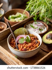 Fit and healthy chilli con carne made from minced turkey meat, kidney beans, pepper, corn and tomatoes. Spicy mexican dish served in a round bowl on a wooden tray. Frontview.
