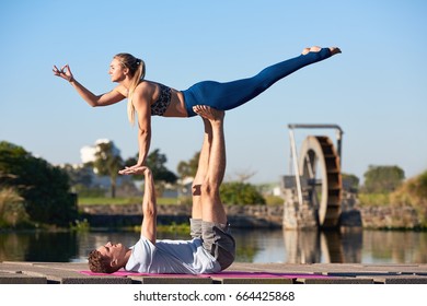 Fit healthy couple doing couples yoga acroyoga outdoors in park with pond - Powered by Shutterstock