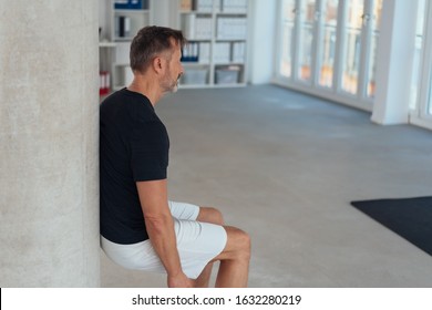 Fit healthy man doing a wall leg sit or squat in an office gym to strengthen and tone his muscles in an active lifestyle concept with copy space - Powered by Shutterstock