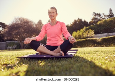 Fit And Healthy Senior Woman In A Pink Sporty Top, Sitting Cross-legged On A Yoga Mat Outdoors, Ready To Do Some Breathing Exercises, With Gentle Morning Sunflare