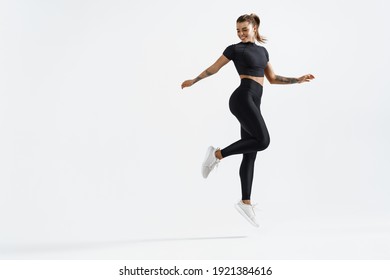 Fit And Healthy Sports Woman Runner Jumping And Looking Behind. Female Athlete In Workout Clothing Doing Exercises On White Background, Staring At Empty Space.