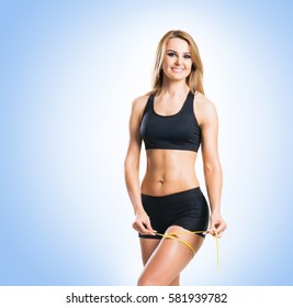 Fit, healthy and sporty woman in sportswear measuring her body over blue background.
