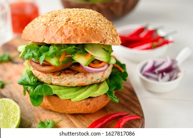 Fit & healthy turkey burger with green avocado, tomatoes and pickled cucumber and carrot, topped with coriander leaves, chilli and served with a sweet and sour sauce.  Oval wooden board, front view. - Powered by Shutterstock