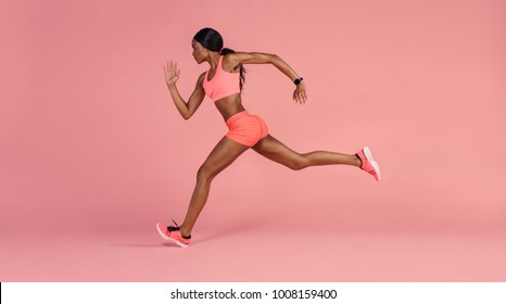 Fit and healthy woman running. African female runner sprinting on pink background.
