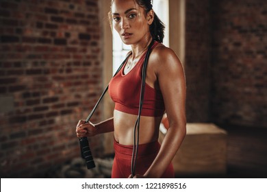 Fit and healthy woman standing at gym with skipping rope. Sportswoman resting after workout.